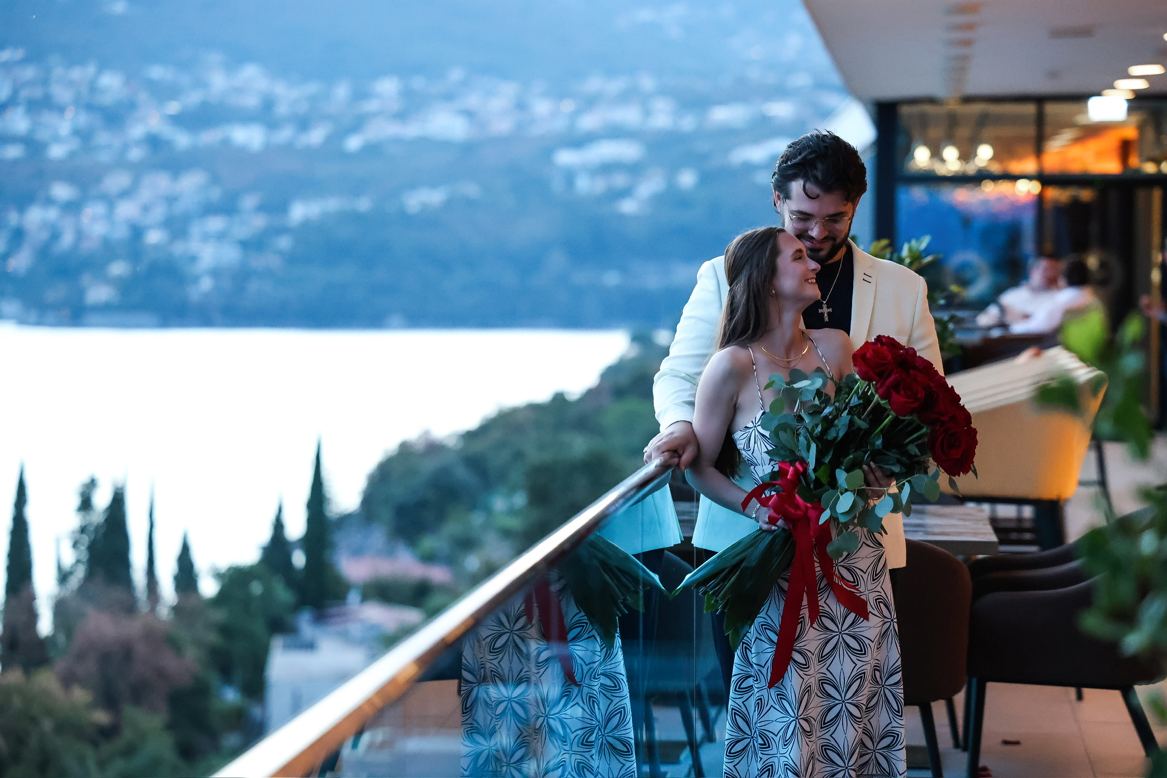 Tatum holding a bouquet of red roses as Zachary embraces her on the balcony